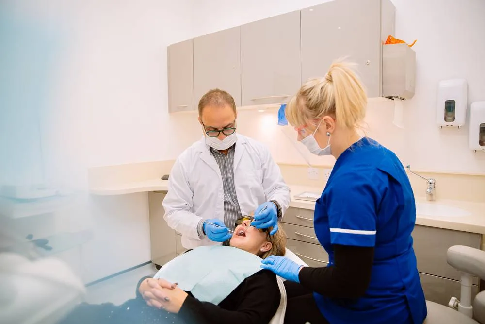 Dentist and dental nurse in blue scrubs treating a patient in the chair