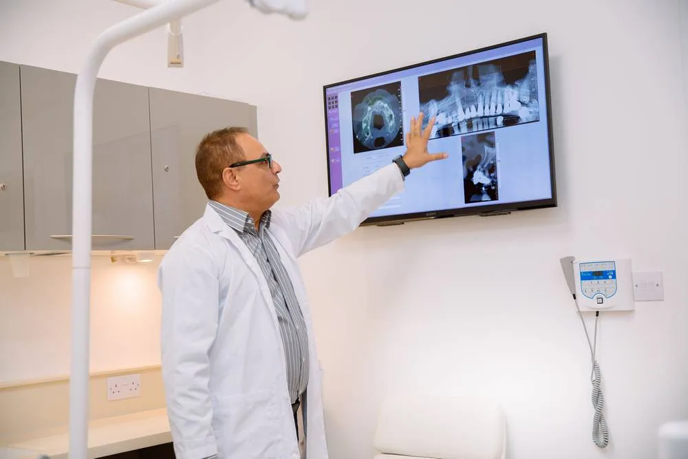 Dentist pointing to a dental X-ray on the wall-mounted surgery screen