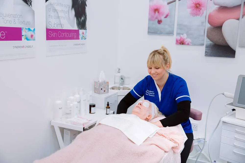 Beauty therapist in blue scrubs giving a client a facial treatment