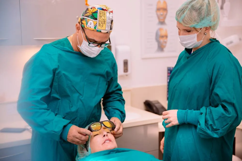 Dentist and dental nurse in surgical scrubs preparing a patient wearing protective glasses